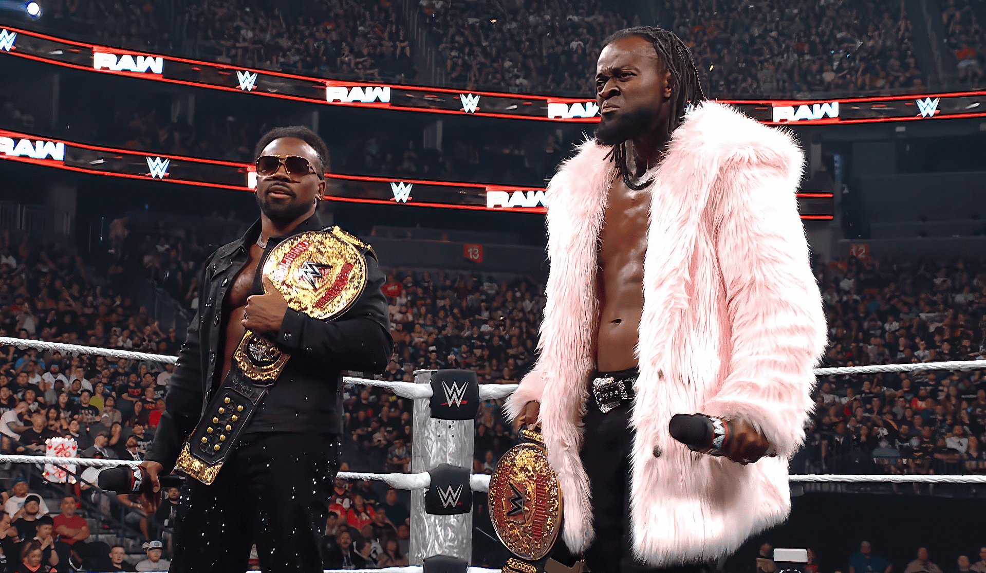 Two WWE wrestlers pose in the ring with championship belts, one wearing a black outfit and sunglasses, the other in a pink fur coat as the crowd roars in the background.